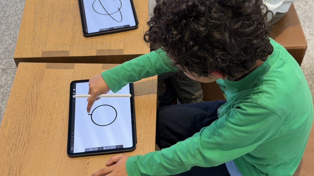 Un bambino disegna con la matita digitale su un iPad appoggiato al tavolo, visto dall’alto