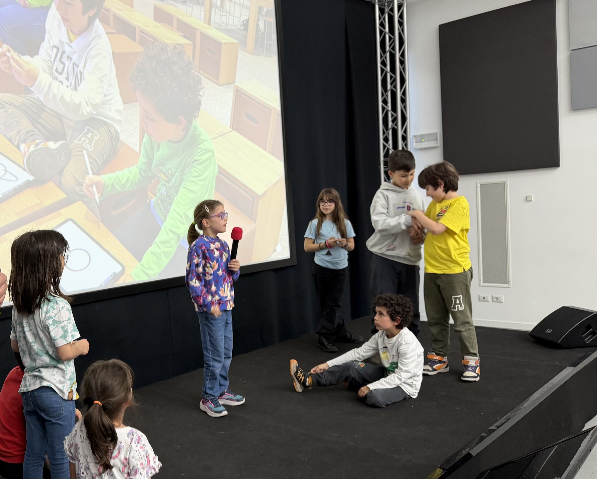 Una bambina al microfono presenta il suo progetto sul palco, davanti ai compagni