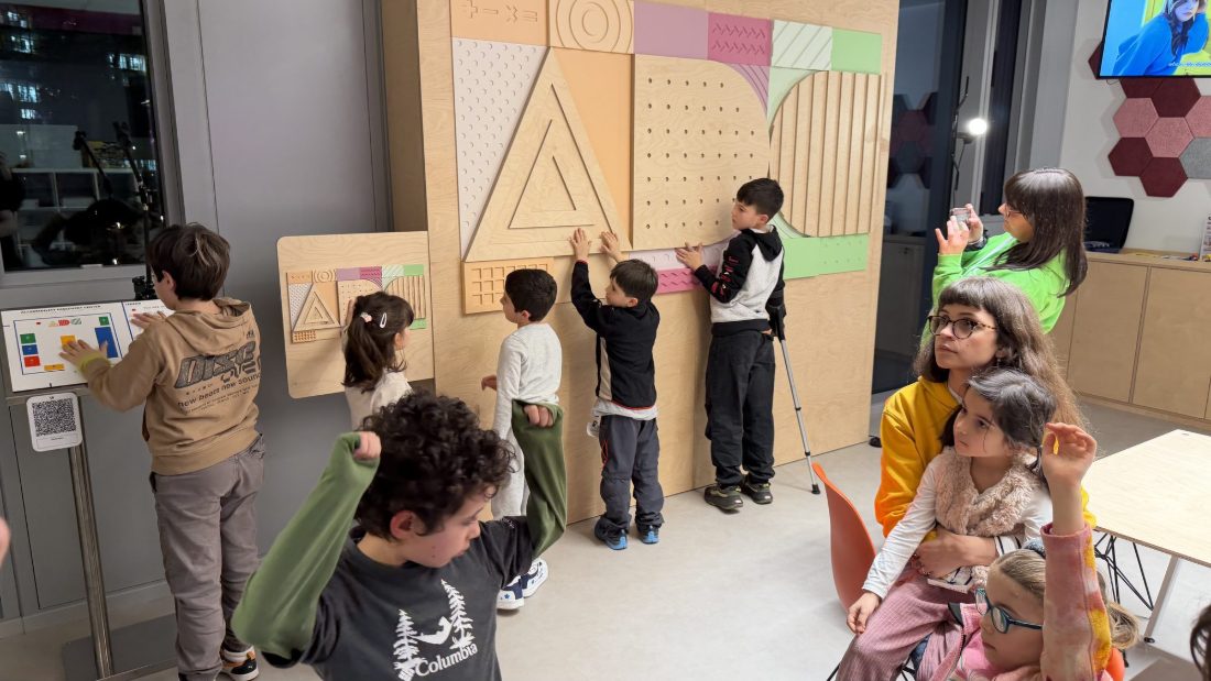 Bambine e bambini toccano i pannelli tattili del centro Google sull’accessibilità; uno di loro cammina con le stampelle