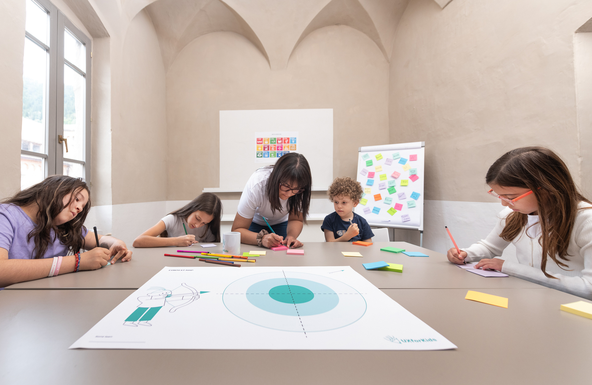 Nina, mentor della School, segue quattro bambini che lavorano sulla mappa del progetto al tavolo dell’aula