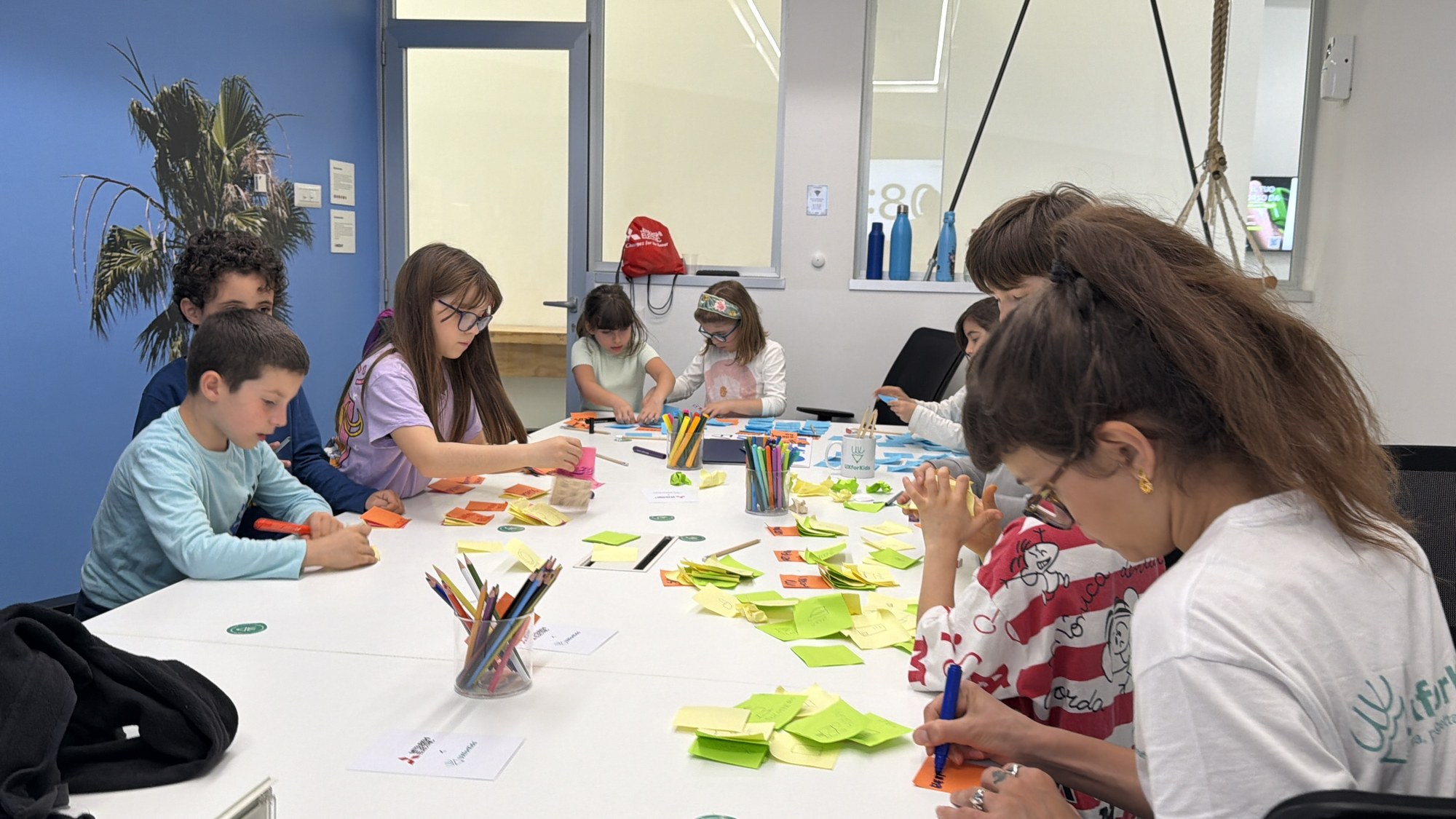 Bambine e bambini progettano in gruppo attorno al tavolo coperto di post-it colorati