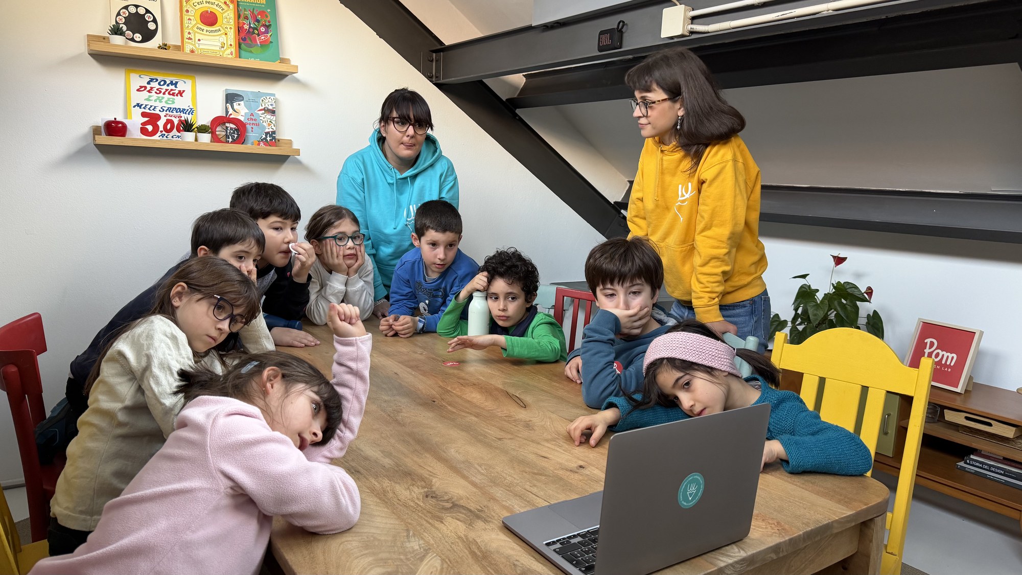 Bambine e bambini attorno a un laptop insieme a due mentor, durante la lezione sull’intelligenza artificiale