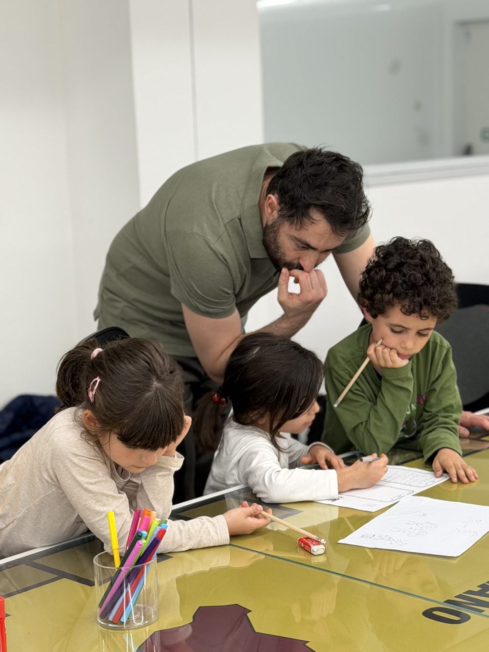 Un mentor chino sul tavolo segue tre bambini che disegnano le loro schermate