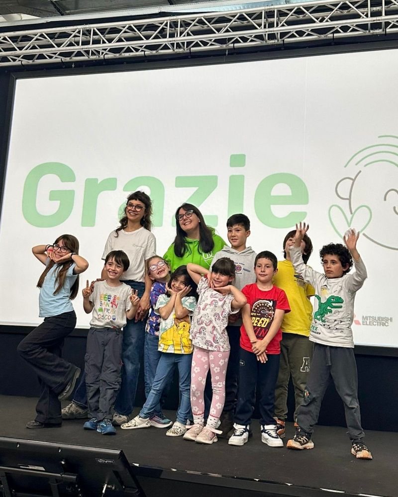 Il gruppo della School in posa sul palco insieme alle mentor, davanti allo schermo con la scritta Grazie